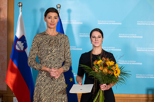 ministrica za pravosodje in generalna državna odvetnica s šopkom in podpisanim dokumentom stojita pred slovensko in evropsko zastavo